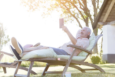 Älterer Mann mit digitalem Tablet, der sich auf einem Liegestuhl im Garten entspannt - CAIF12704