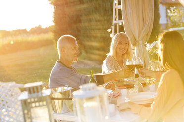 Senior couple an adult daughter toasting wine glasses at sunny patio table - CAIF12706