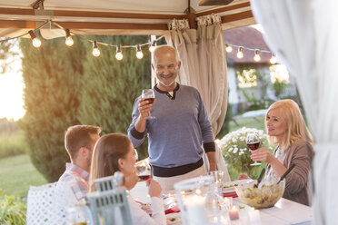 Senior man toasting family with red wine at patio table - CAIF12707