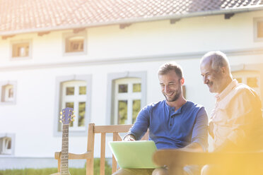 Vater und erwachsener Sohn benutzen Laptop auf einer Gartenbank - CAIF12709