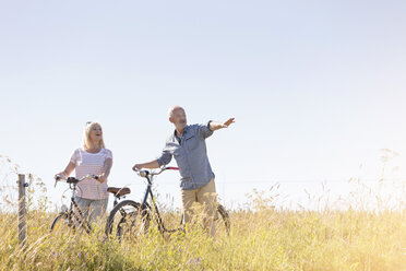 Senior couple bike riding in sunny rural field under blue sky - CAIF12722