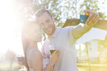 Young couple with wine taking selfie in sunny backyard - CAIF12726