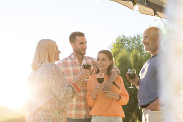 Family talking and drinking wine on sunny patio - CAIF12729