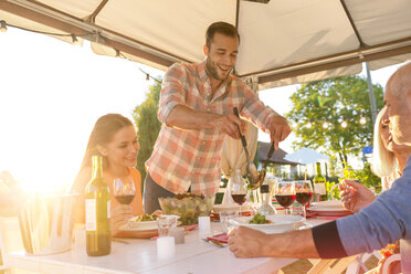 Man serving salad at sunny patio table - CAIF12731