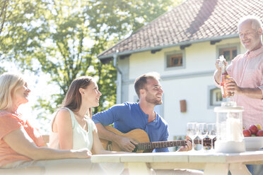 Vater öffnet eine Flasche Roséwein für die Familie am sonnigen Terrassentisch - CAIF12733