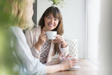 Lächelnde Frauen trinken Kaffee am Fenster eines Cafés - CAIF12742