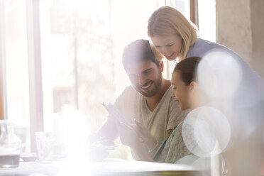 Familie benutzt digitales Tablet in einem sonnigen Cafe - CAIF12746