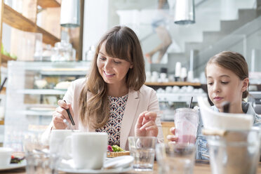 Mother and daughter eating and drinking at cafe table - CAIF12770