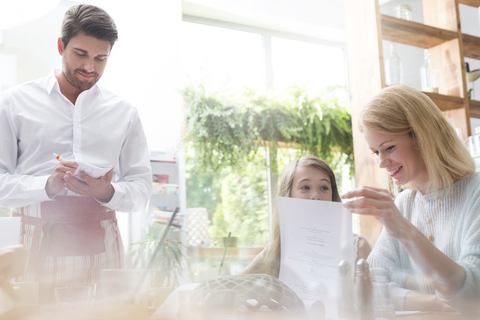 Kellner nimmt die Bestellung von Mutter und Tochter in einem Café auf, lizenzfreies Stockfoto