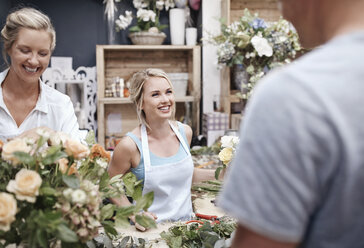 Floristen arrangieren Blumensträuße und sprechen mit Kunden im Blumenladen - CAIF12790