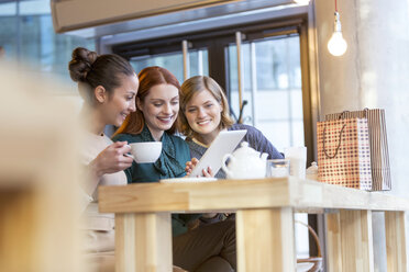 Lächelnde Frauen trinken Tee und teilen sich ein digitales Tablet am Café-Tresen - CAIF12798