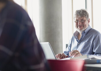 Porträt eines lächelnden Mannes, der an einem Laptop in einem Klassenzimmer der Erwachsenenbildung arbeitet - CAIF12854