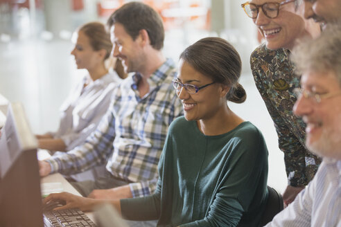 Lächelnde Studenten der Erwachsenenbildung arbeiten gemeinsam am Computer im Klassenzimmer - CAIF12867