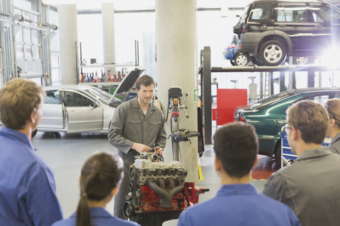 Mechaniker erklärt Studenten in einer Autowerkstatt den Motor eines Autos, lizenzfreies Stockfoto