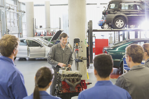 Mechaniker erklärt Studenten in einer Autowerkstatt den Motor eines Autos - CAIF12877