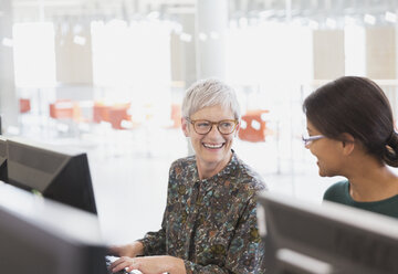 Smiling women talking at computers in adult education classroom - CAIF12879