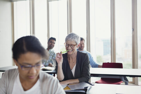 Lächelnde ältere Frau, die im Klassenzimmer der Erwachsenenbildung lernt - CAIF12884