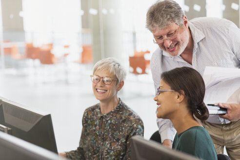 Lächelnde Studenten, die sich in einem Klassenzimmer der Erwachsenenbildung am Computer unterhalten - CAIF12892