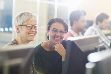 Lächelnde Frauen am Computer in einem Klassenzimmer der Erwachsenenbildung - CAIF12910