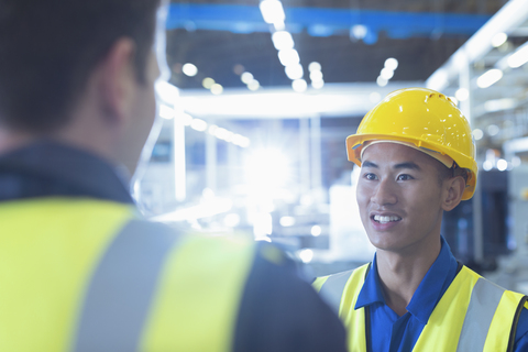 Arbeiter in reflektierender Kleidung im Gespräch in einer Fabrik, lizenzfreies Stockfoto