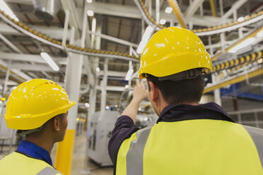 Workers discussing printing press conveyor belts overhead - CAIF12954