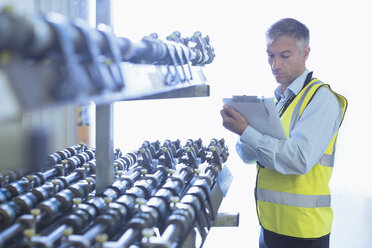 Ingenieur mit Klemmbrett bei der Kontrolle des Förderbands einer Druckmaschine - CAIF12959