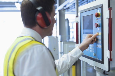 Arbeiter mit Gehörschutz am Bedienpult einer Maschine - CAIF12971