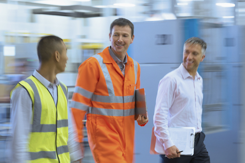 Arbeiter in reflektierender Kleidung gehen in einer Fabrik, lizenzfreies Stockfoto