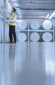 Worker examining large paper spools in printing plant - CAIF12987