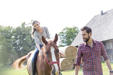 Mann führt Frau beim Reiten auf einer ländlichen Weide, lizenzfreies Stockfoto