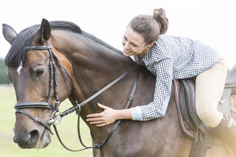 Lächelnde Frau reitet anlehnend und streichelt Pferd, lizenzfreies Stockfoto