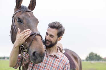 Lächelnder Mann umarmt Pferd - CAIF13024