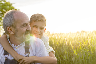 Portrait affectionate grandson hugging grandfather in rural wheat field - CAIF13030