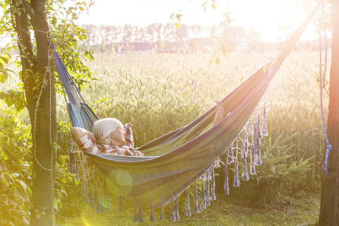 Serene woman napping in hammock next to sunny rural wheat field stock photo