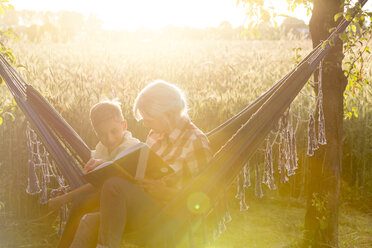 Grandmother and grandson reading book in sunny rural hammock - CAIF13042
