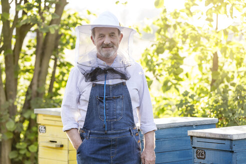 Porträt eines selbstbewussten Imkers mit Schutzhut neben den Bienenstöcken - CAIF13044