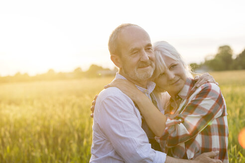Zärtliches, gelassenes älteres Paar, das sich in einem sonnigen ländlichen Weizenfeld umarmt - CAIF13054