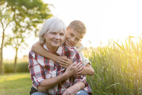 Porträt lächelnd Großmutter und Enkel umarmen in der Nähe sonnigen ländlichen Weizenfeld - CAIF13056