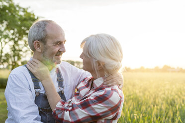 Affectionate senior couple hugging in sunny rural wheat field - CAIF13063