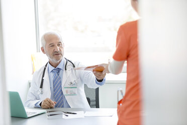 Doctor at desk giving medical record to nurse in doctor’s office - CAIF13071