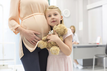 Portrait Mädchen mit Teddybär, das seine schwangere Mutter in der Arztpraxis umarmt - CAIF13076
