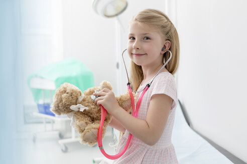 Portrait smiling girl using stethoscope on teddy bear in examination room - CAIF13078