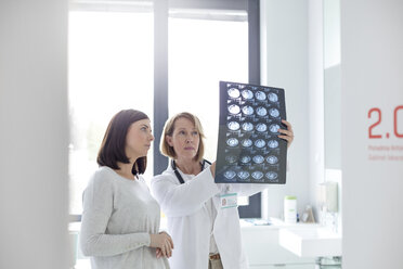 Serious doctor and patient reviewing x-rays in examination room - CAIF13084