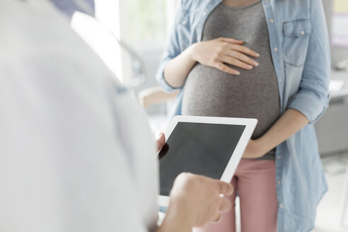 Arzt mit digitalem Tablet im Gespräch mit schwangerer Patientin - CAIF13086