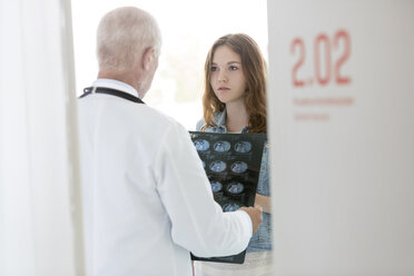 Arzt bespricht Röntgenbilder mit ernstem jugendlichen Patienten im Untersuchungsraum - CAIF13087
