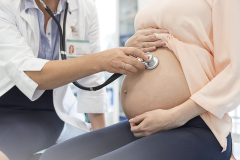 Doctor using stethoscope on pregnant patient’s stomach stock photo