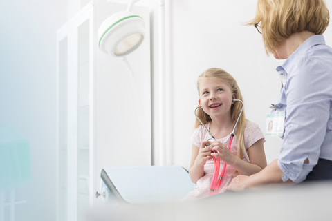 Pediatrician watching girl patient playing with stethoscope in examination room stock photo