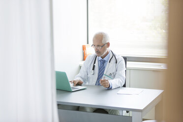 Doctor working at laptop in doctor’s office - CAIF13097