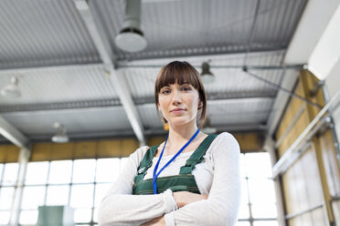 Porträt einer ernsthaften Arbeiterin mit verschränkten Armen in einer Fabrik - CAIF13109