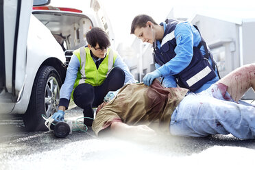 Rescue workers tending to car accident victim in road - CAIF13115